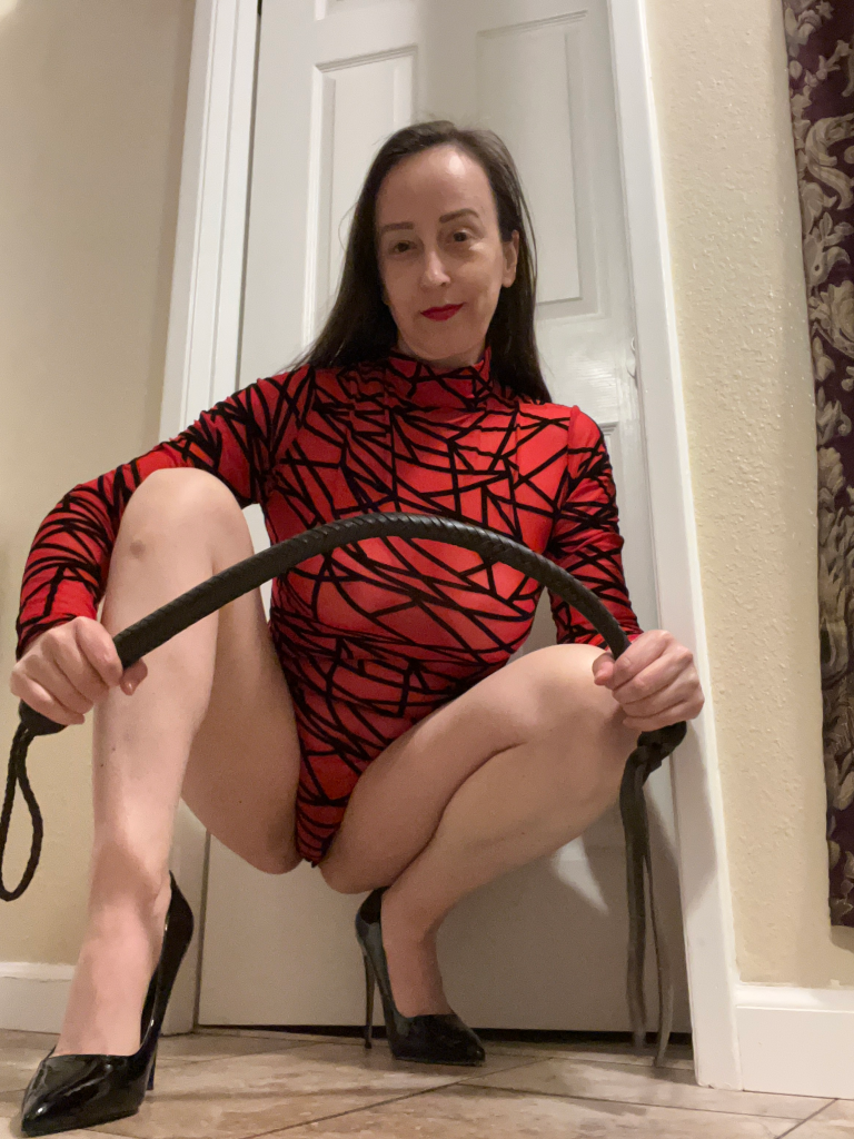Dominatrix in a red and black bodysuit holding a quirt